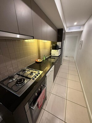 A modern kitchen with a gas stove, microwave, and a small sink. - Cozy & Affordable in CBD - Free Wine (Adelaide)