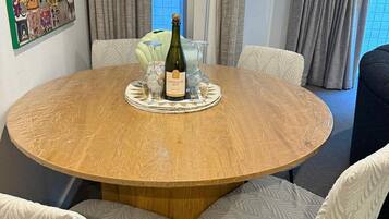 A round wooden table with a bottle of champagne and four glasses, surrounded by white upholstered chairs with a leaf pattern.