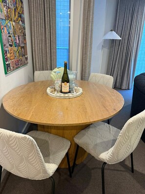 A round wooden table with a bottle of champagne and four glasses, surrounded by white upholstered chairs with a leaf pattern. - Cozy & Affordable in CBD - Free Wine (Adelaide)