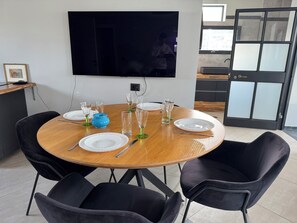 Une table de salle à manger ronde, avec de l’assiette blanche, des verres transparents et un vase bleu.