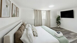 Una camera d'albergo moderna con un letto, una TV a schermo piatto, una pianta in vaso e opere d'arte alle pareti.