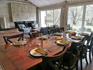 A dining area with a wooden table set for six, surrounded by chairs, with a view of trees through large windows. - Holiday Home “Les Pyrénées Au Bord De l’Eau” with Lake View, Private Terraces & Wi-Fi (Barbazan)