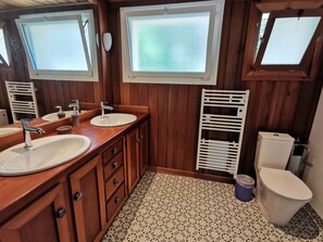 A bathroom with wooden paneling, two sinks, a mirror, a toilet, and a window. - Holiday Home “Les Pyrénées Au Bord De l’Eau” with Lake View, Private Terraces & Wi-Fi (Barbazan)