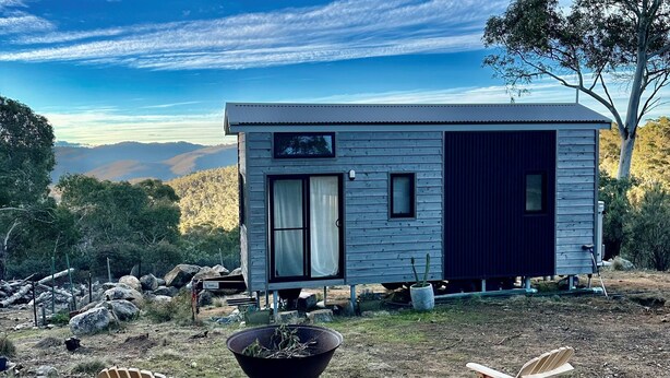 Une petite cabane à un seul étage, avec une porte d’entrée sombre, une fenêtre et un petit porche.
