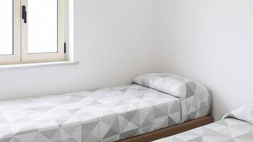 A bedroom with two single beds, a window with a wooden frame, and a plain white wall.
