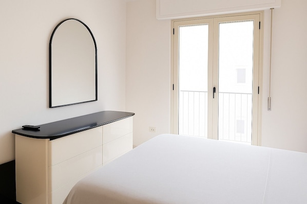 Une chambre à coucher avec un lit, une commode, un miroir et une porte donnant sur un balcon.