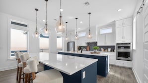 Una cocina moderna con una isla central, armarios blancos e iluminación colgante.