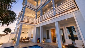Una casa de varios niveles con piscina, mobiliario exterior y un balcón con luces colgantes.