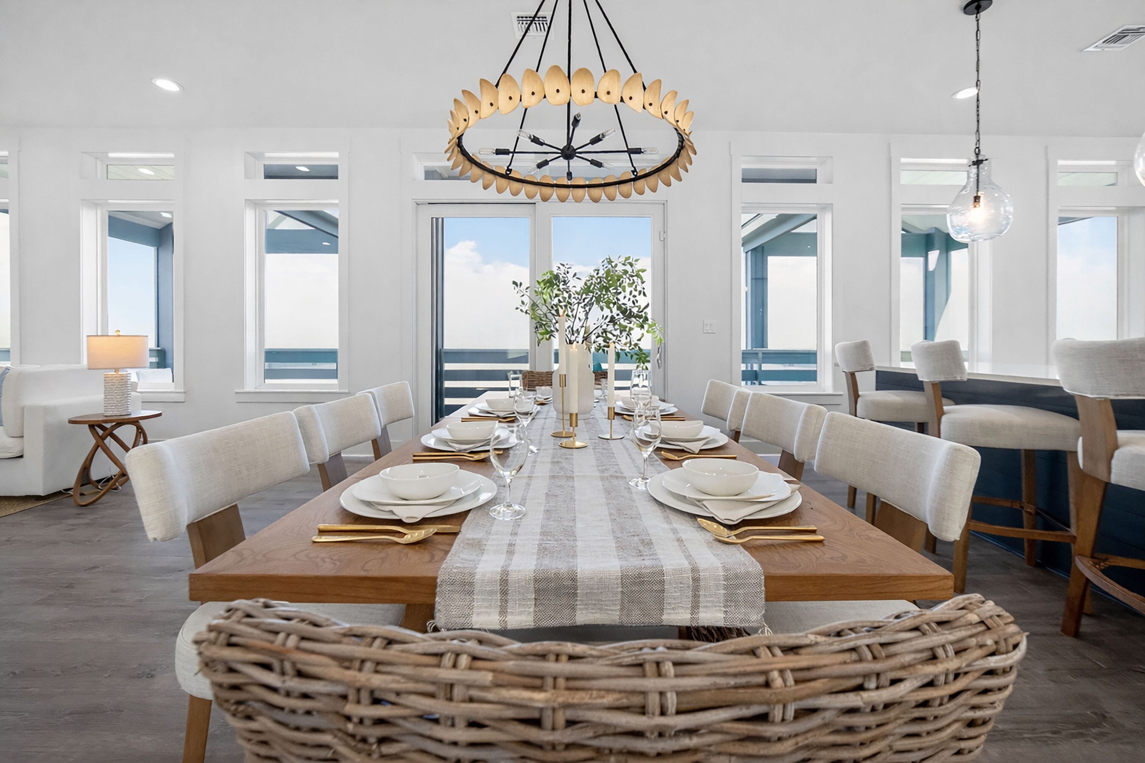 Comedor con una larga mesa dispuesta para seis comensales, rodeada de sillas, una araña y vistas al exterior.