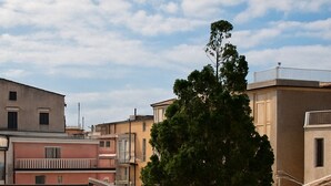 A balcony with a tiled floor and a metal railing overlooking a residential area with buildings and a tree. - Appatamenti ABR Corso - Apartment with View and Balcony (Le Castella)
