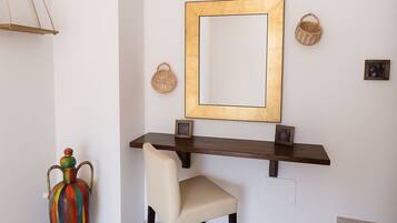 Ein modernes Interieur mit einem dunklen Holzkonsole, einem beigen Sessel, einer farbenfrohen Vase und einem großen Spiegel mit goldener Rahmung.