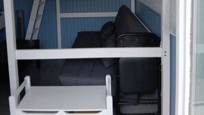 A bunk bed with a desk and ladder, a blue wall, and a window.