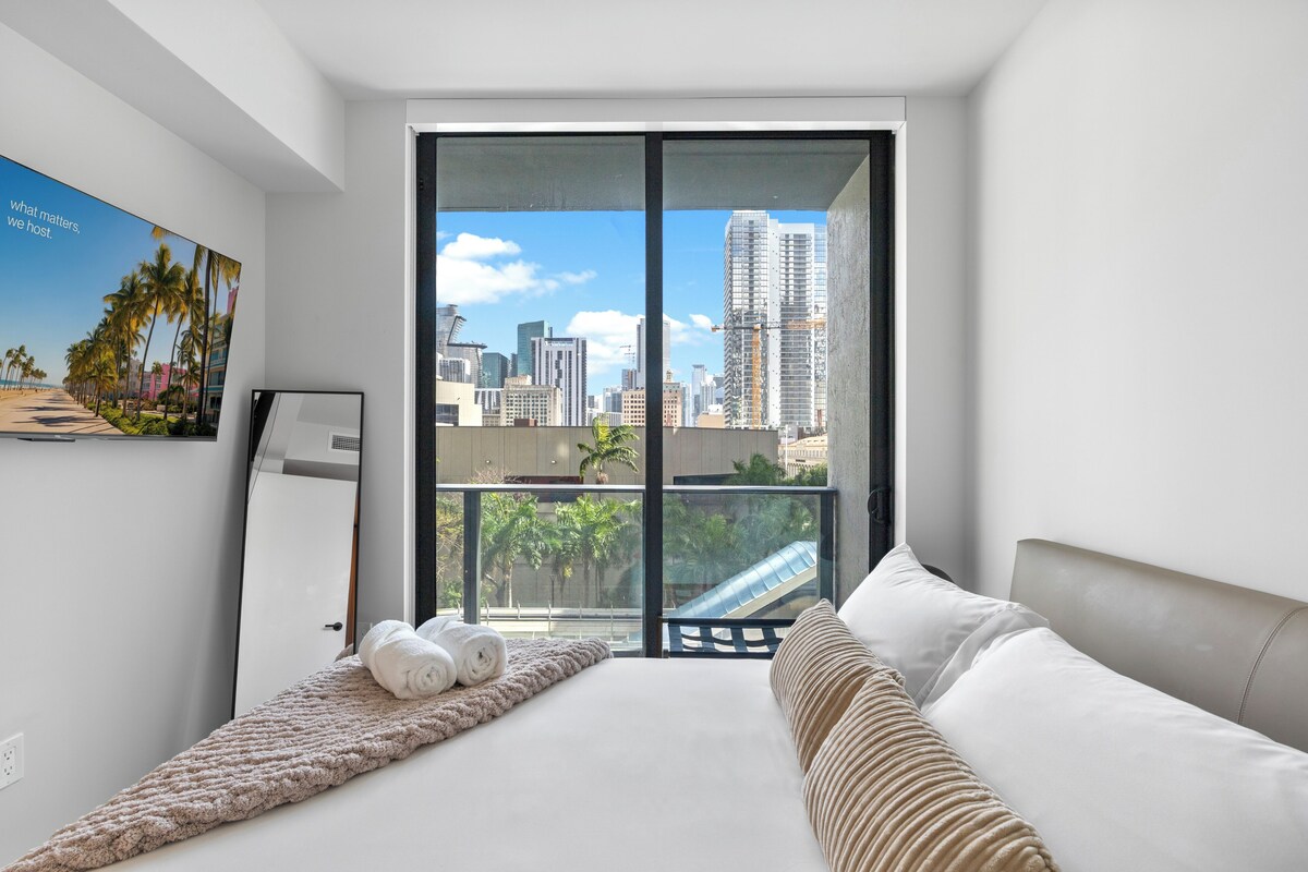 A modern hotel room with a large bed, a view of the cityscape, and a balcony.