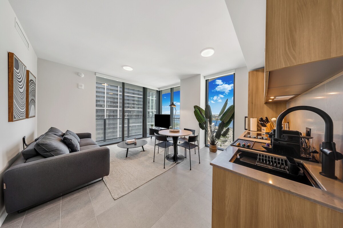 A modern apartment with a sofa, dining table, kitchen, and large windows.