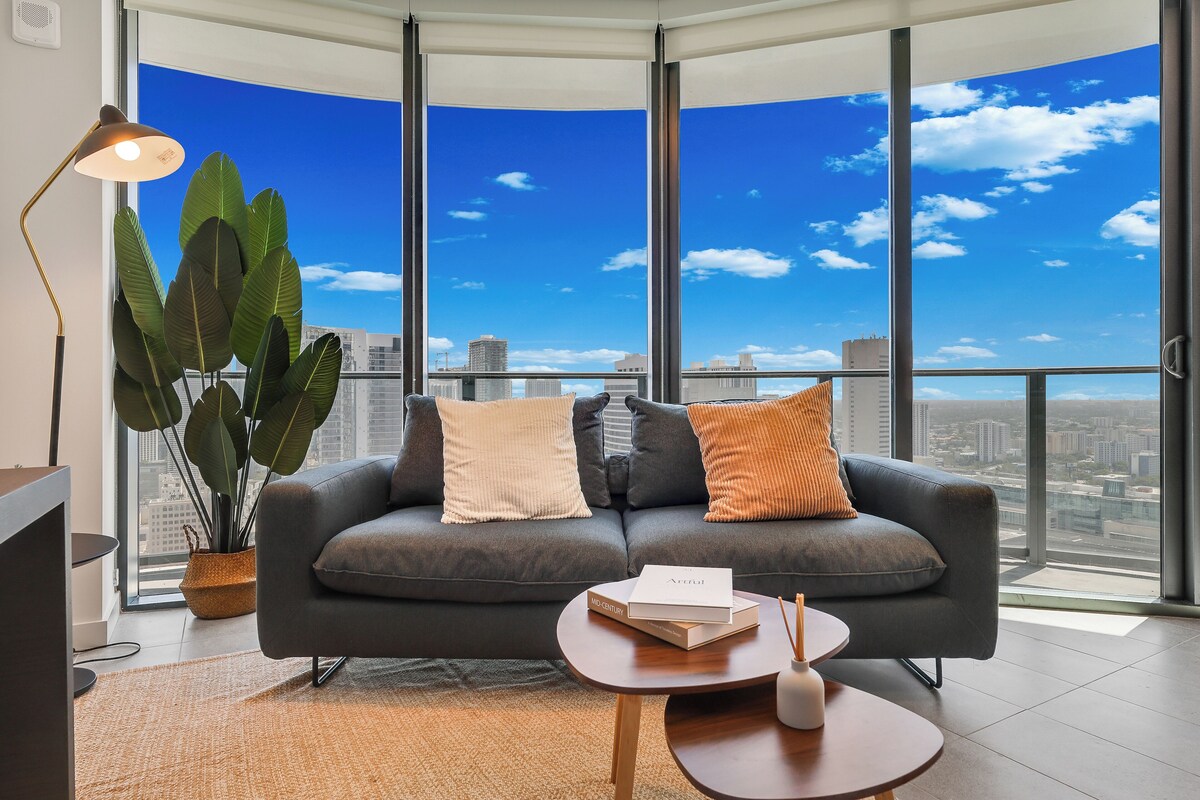 A modern living room with a large window, a sofa, a coffee table, and a plant.