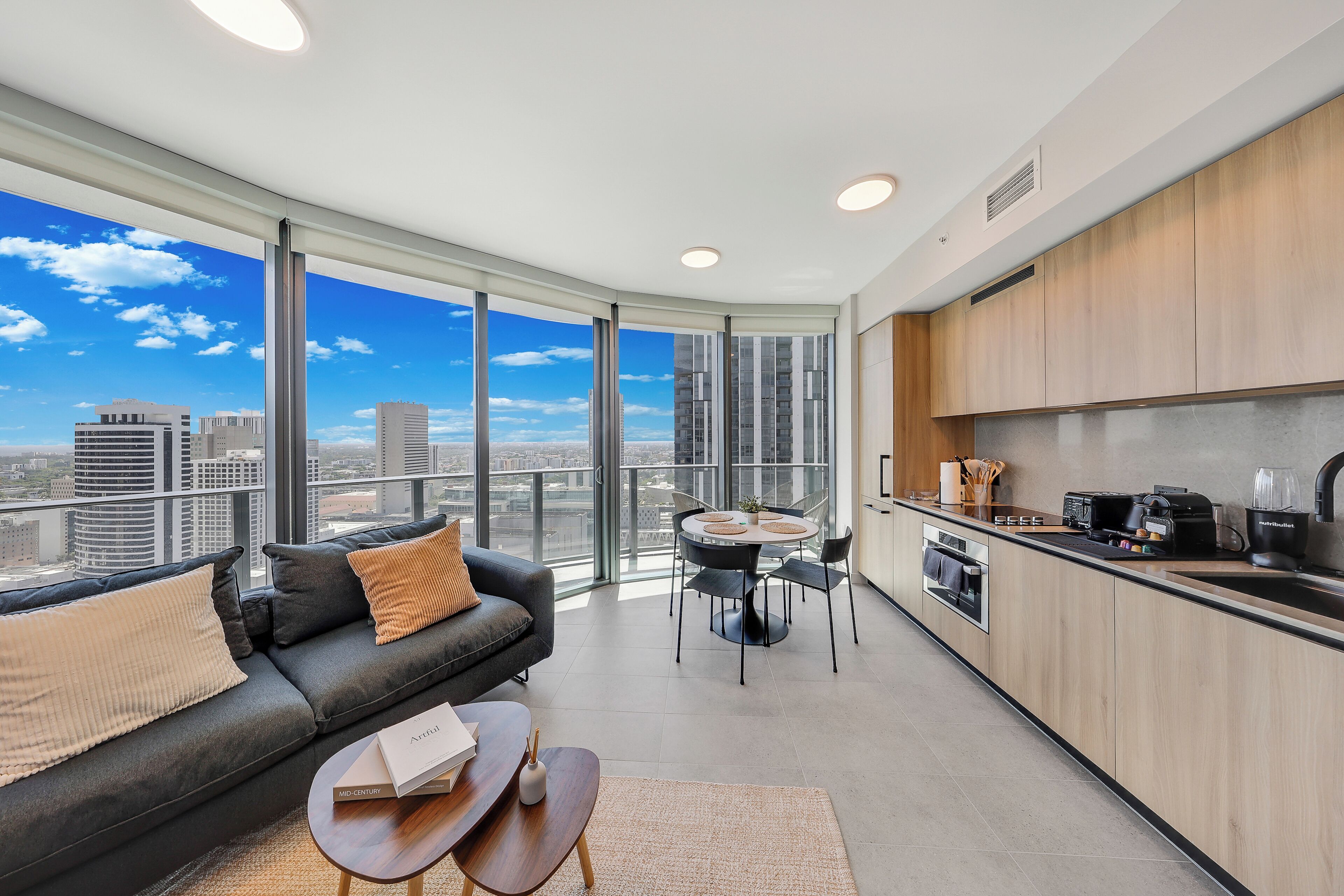 A modern apartment with a living area, kitchen, and large windows offering a city view.