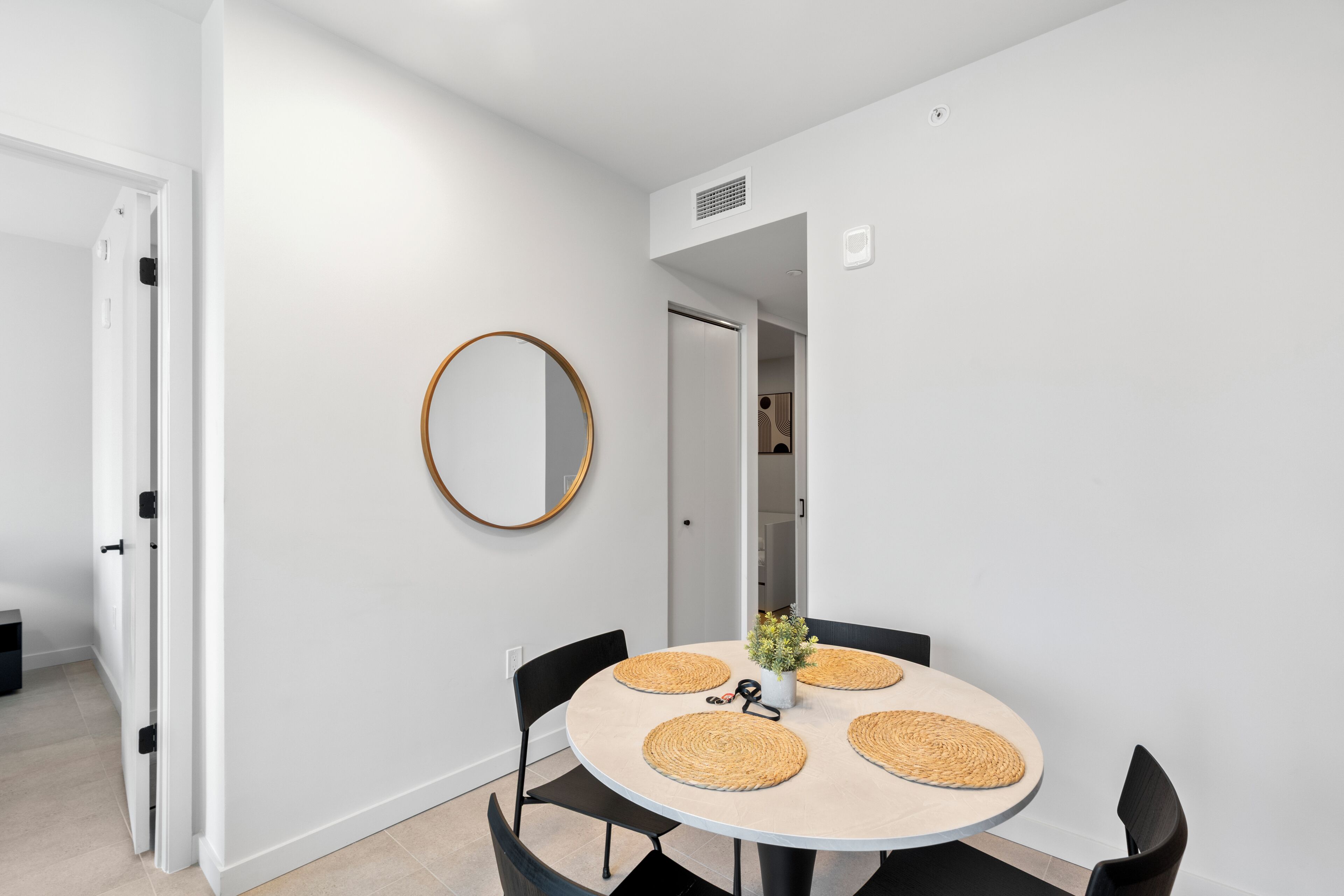 A modern dining area with a round table, black chairs, and a round mirror on the wall.