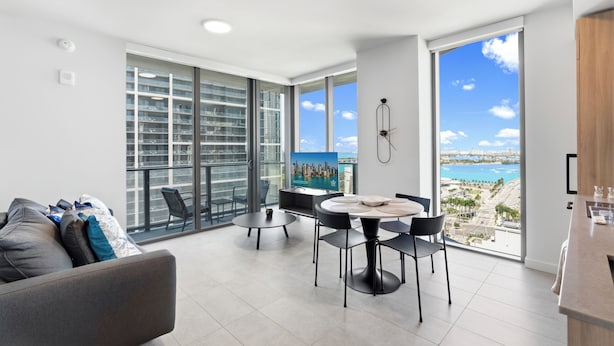 A modern living room with a balcony, a dining area, and a large TV screen. - First Residences - Heart of Miami - We Host (Miami)
