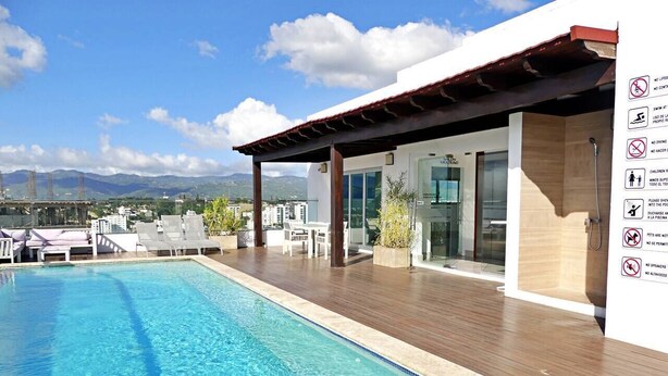 Una piscina con cubierta de madera, sillas de descanso y vistas a montañas.