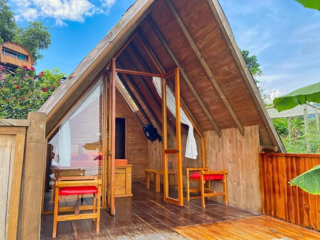 Una estructura de madera con techo inclinado, puerta de vidrio y un pequeño espacio de estar con bancos y una mesa.