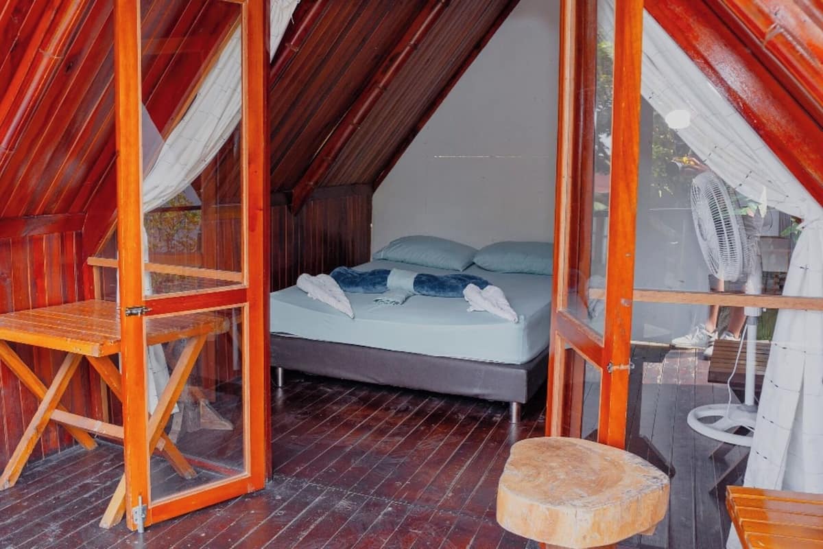 A cozy room with a bed, a small table, and a fan.