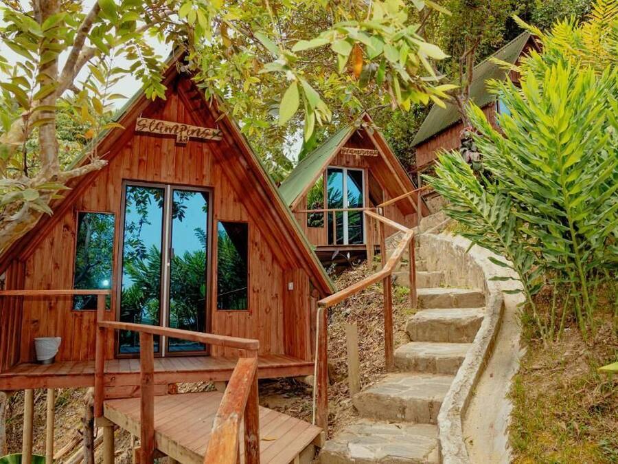 Dos cabañas de madera con ventanas amplias, una terraza de madera y una escalera de piedra.