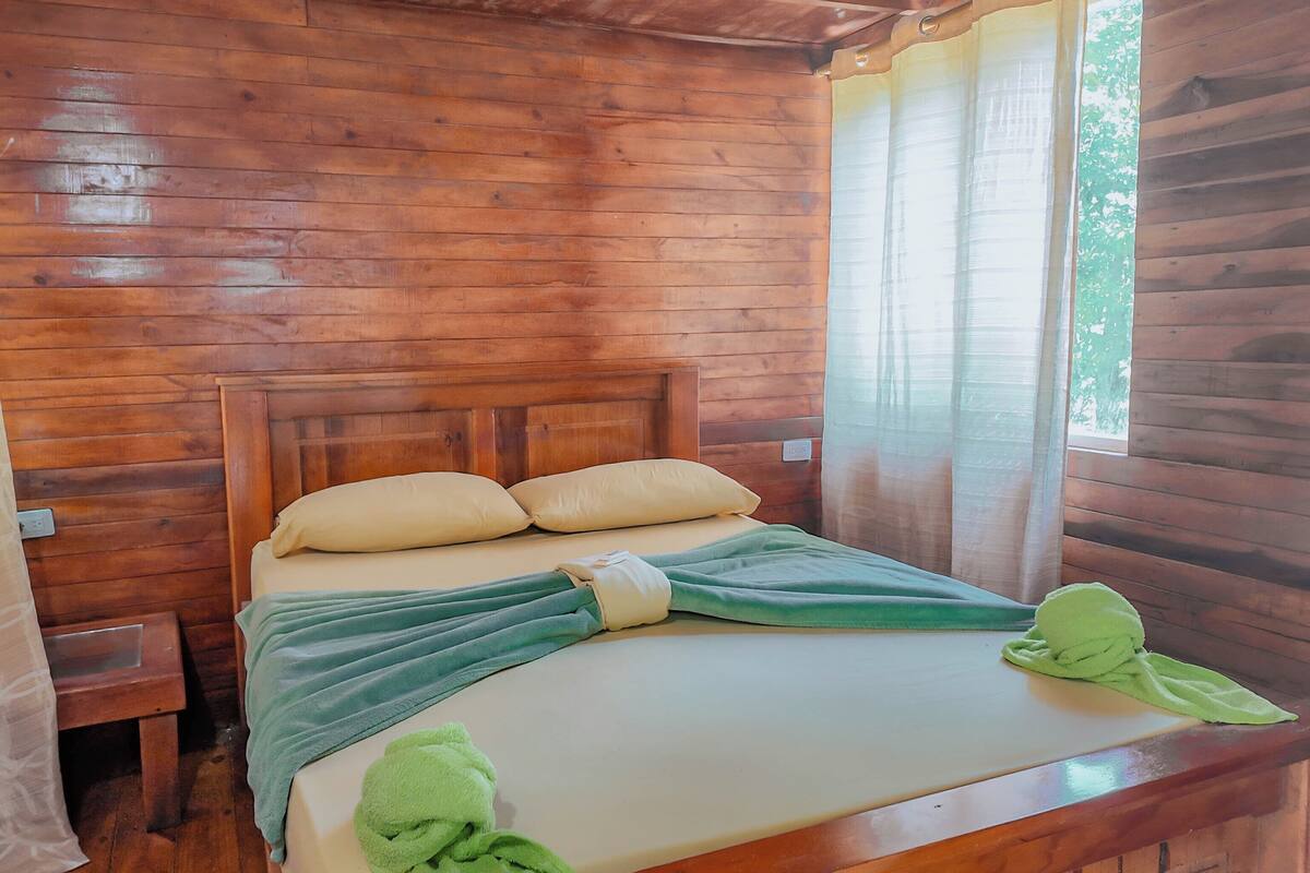 A wooden room with a bed, curtains, and a window.