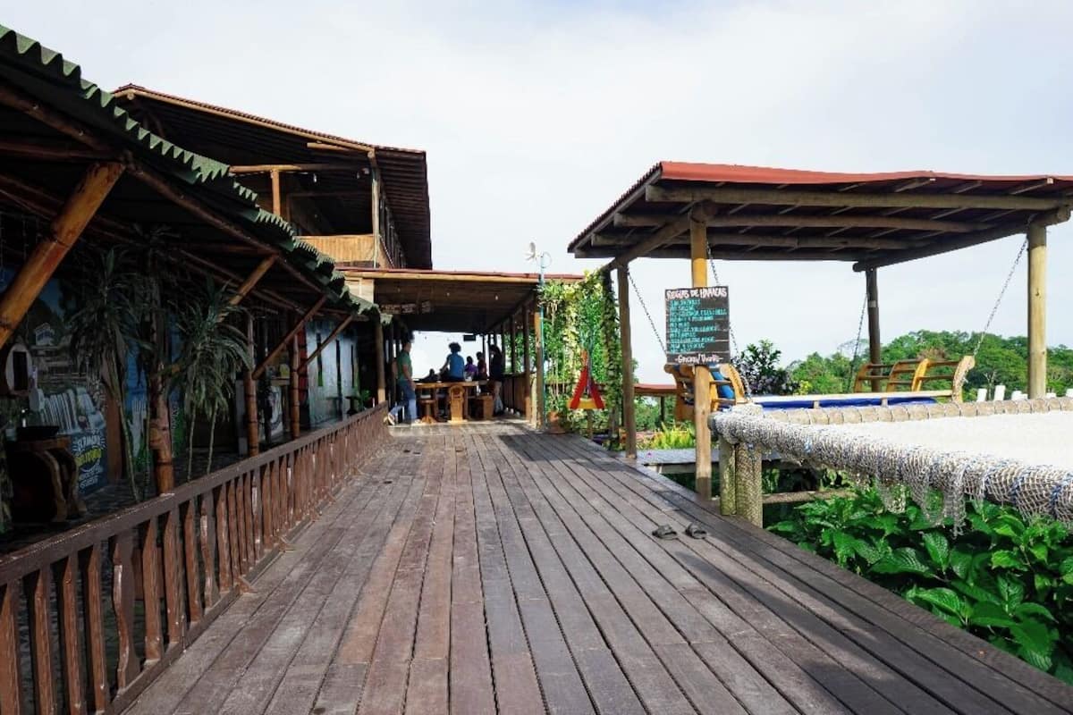 A wooden deck leading to a restaurant with outdoor seating, a signboard, and a view of the sea.