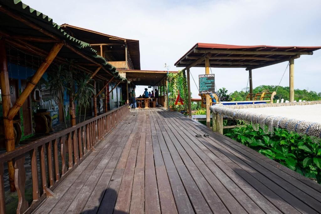 A wooden deck leading to a restaurant with outdoor seating, surrounded by greenery.