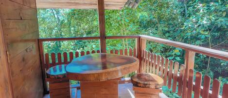A wooden deck with a round table and benches, surrounded by a wooden fence, overlooking a lush green forest.