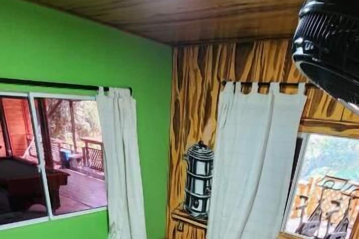 A room with a bed, a window with curtains, a wooden wall, and a tiled floor.