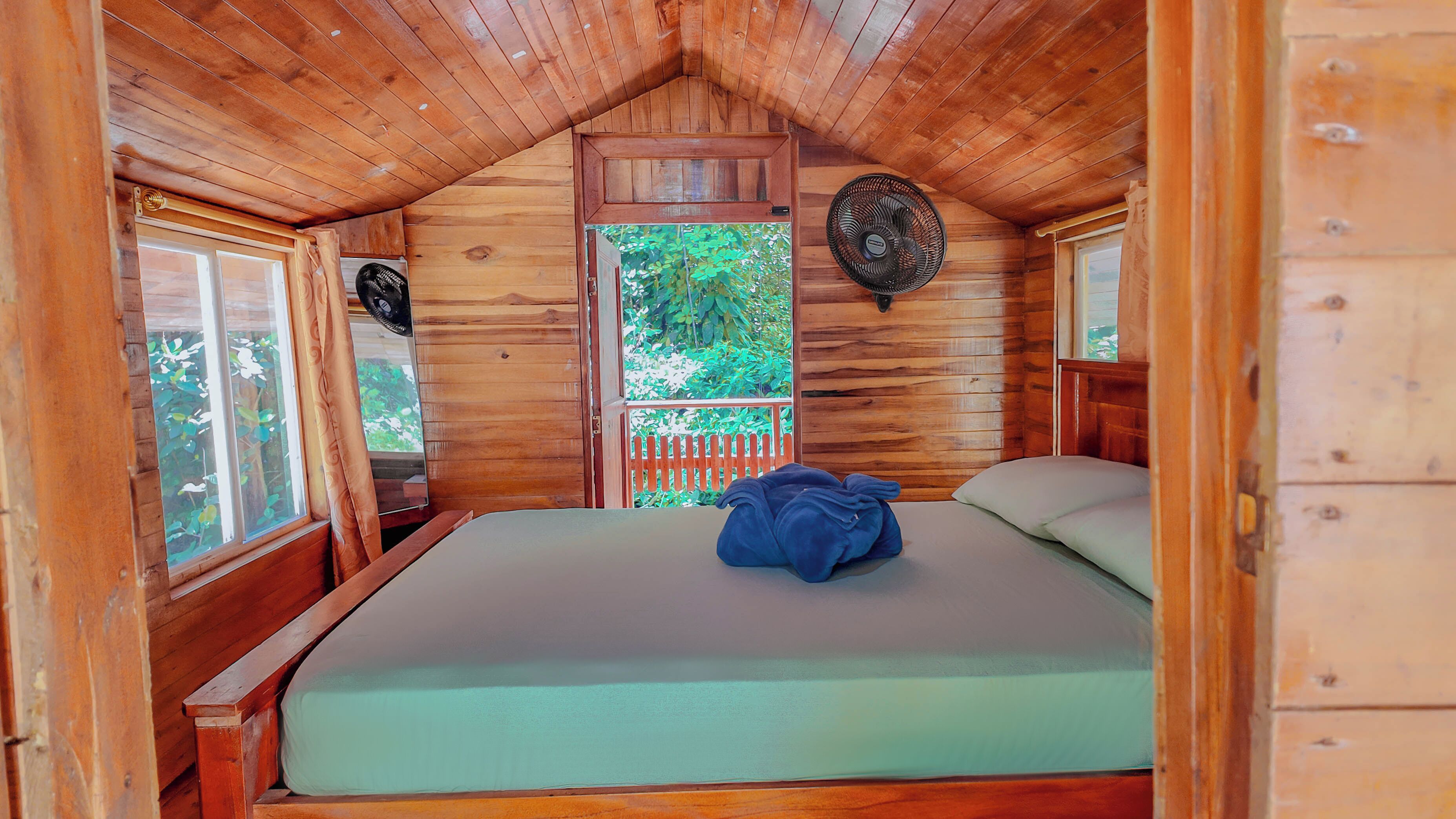Une pièce de cabane en bois comprenant un lit, une fenêtre et un ventilateur.