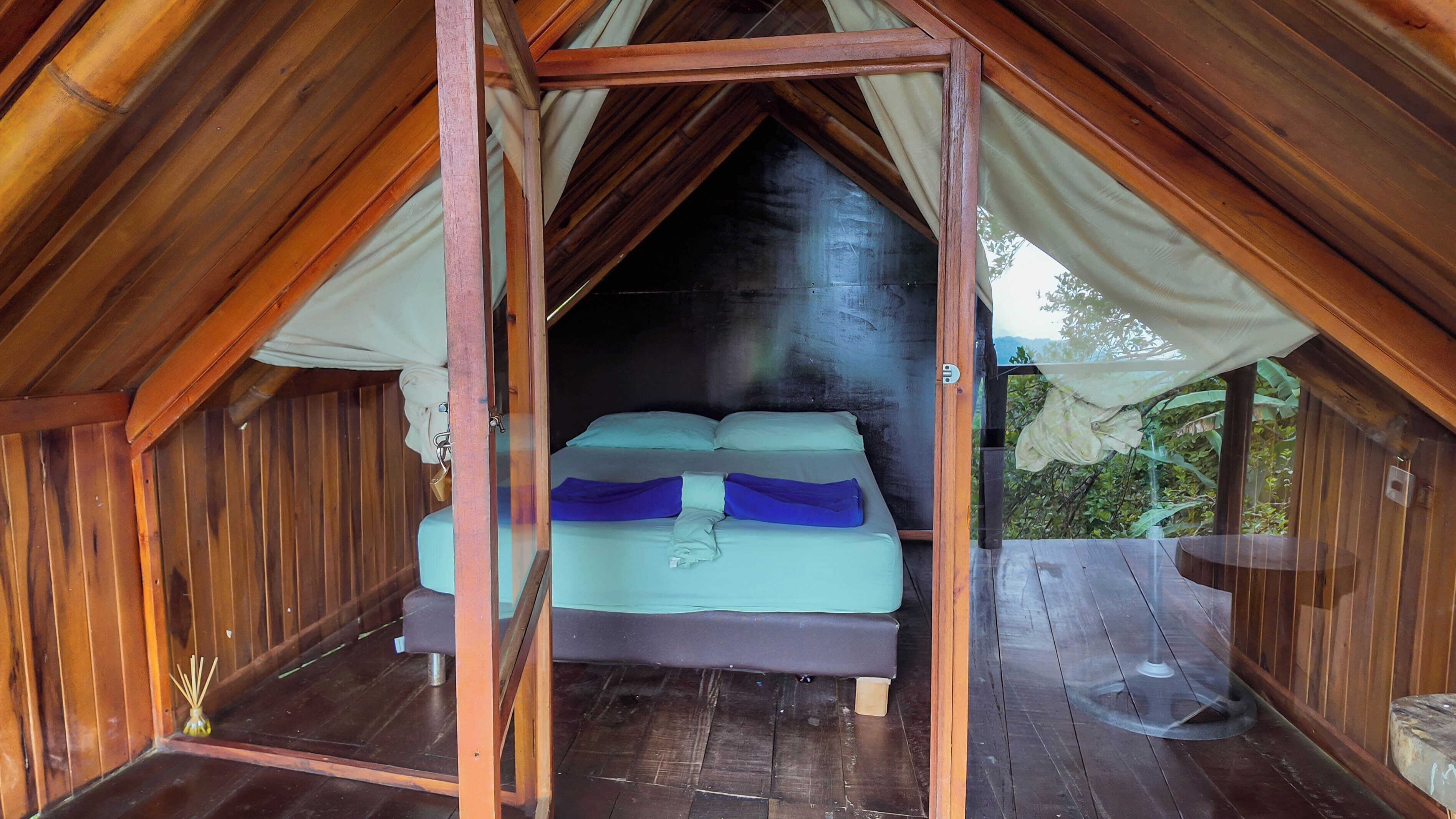 Una stanza in legno con un letto, tende e vista su del verde all'esterno.
