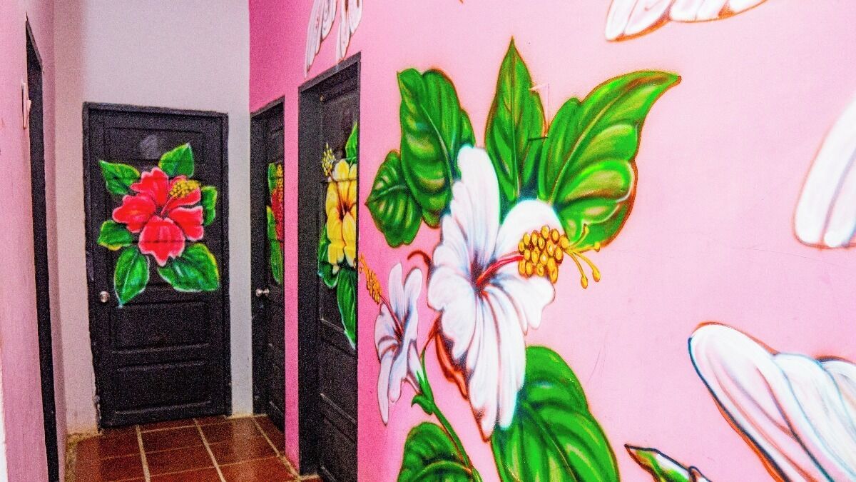 Un pasillo con dos puertas negras, una con un mural de flores rojas y otra con un mural de flores blancas.