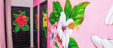 Un pasillo con dos puertas negras, una con un mural de flores rojas y otra con un mural de flores blancas.