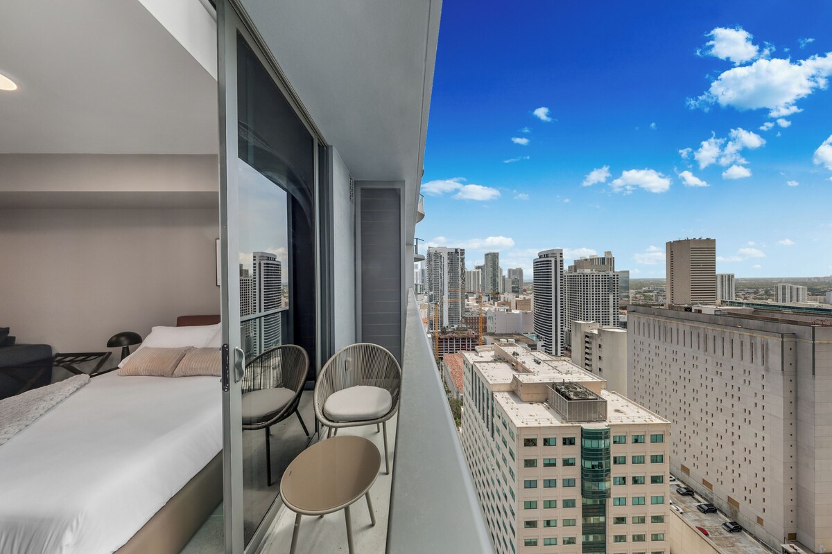 Ein Hotelzimmer mit Bett, zwei Stühlen, einem Tisch und Blick auf die Stadt.