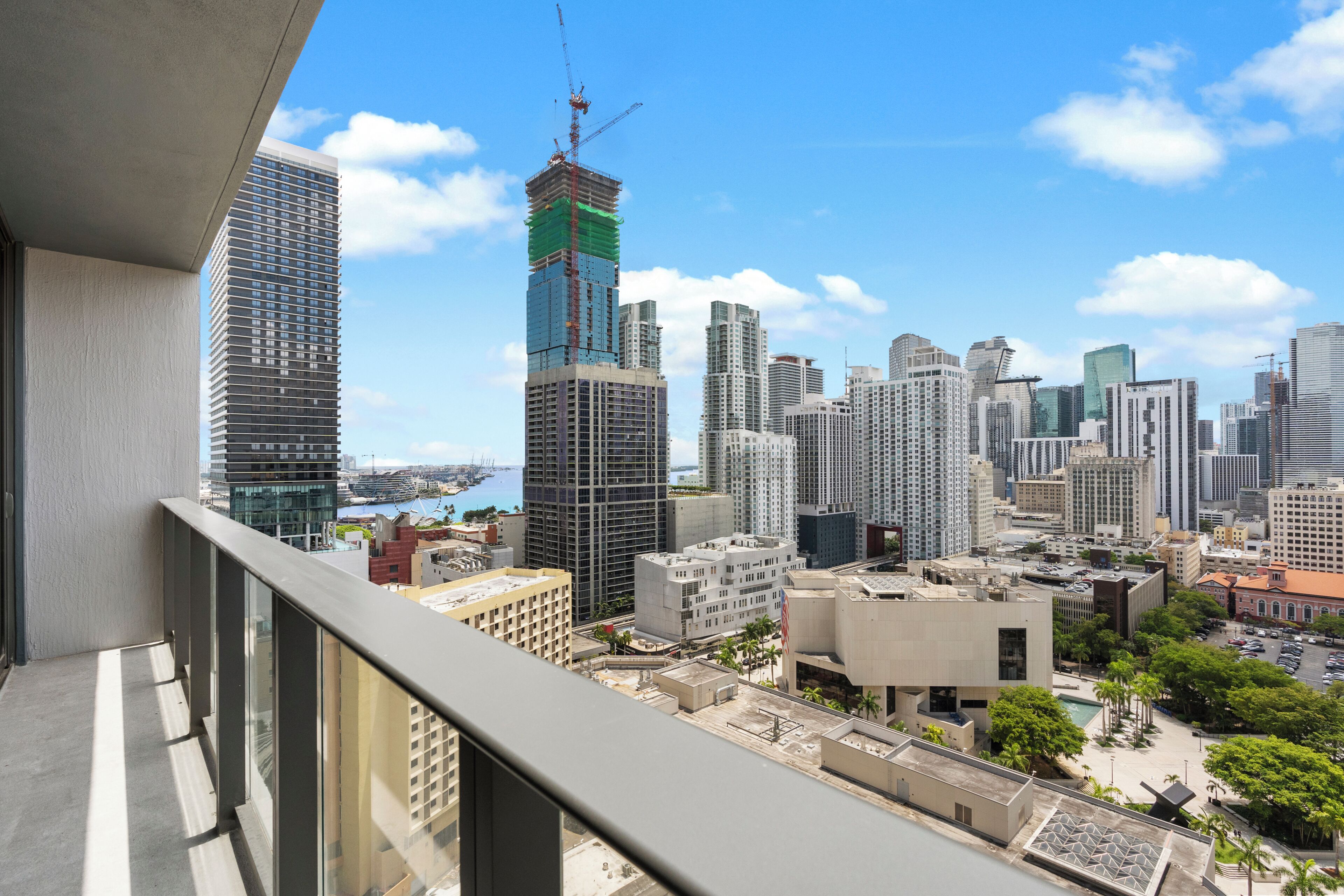 Un immeuble de grande hauteur avec une grue de construction, un ciel bleu dégagé et un paysage urbain composé de différents bâtiments.