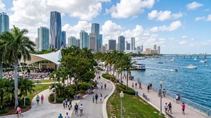 Eine Uferpromenade mit Stadtansicht, Palmen und einer weißen Markise.