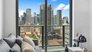 A modern living room with a large window, a grey sofa, and a small table with decorative items. - 501 Building - Close to Kaseya Center - We Host (Miami)