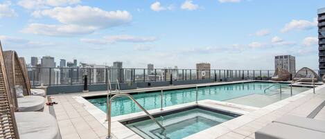 Una piscina en la azotea con sillones de descanso, vista al horizonte urbano y cielo despejado.
