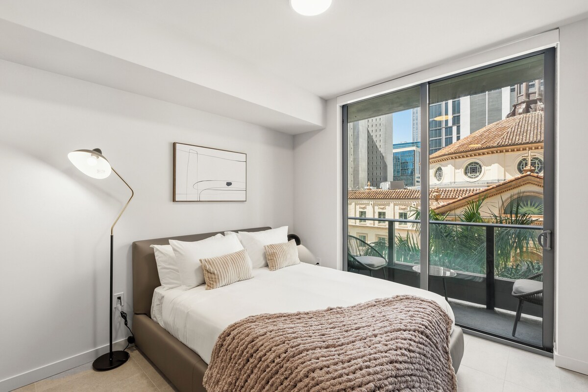 Ein modernes Schlafzimmer mit einem großen Bett, einer Stehlampe, einem gerahmten Bild und einem Balkon mit Blick auf die Stadt.