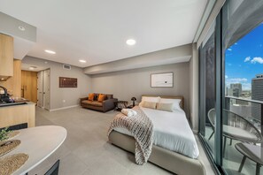 Ein modernes Hotelzimmer mit Bett, einer Couch, einem Esstisch und Blick auf die Stadt durch große Fenster.