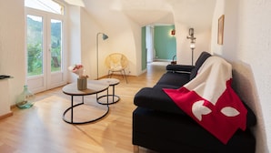 Een moderne woonkamer met een bank, een ronde tafel, een rieten stoel en uitzicht door een glazen deur.