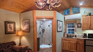 Accogliente interno di una baita con soffitto in legno, camino, divano, tappeto decorato, cucina con mobili in legno e zona doccia.