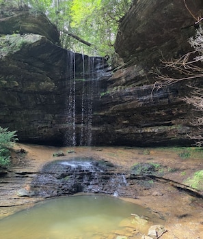 A waterfall cascading into a pool surrounded by rocky cliffs and greenery.