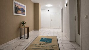 Een hal met een gekaderd schilderij aan de muur, een klein tafeltje met een plant en een vloerkleed met het AR Living logo.