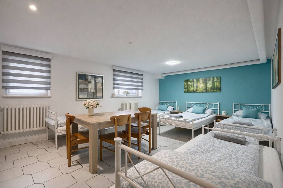 Quarto com mesa de jantar, quatro camas e uma parede azul.