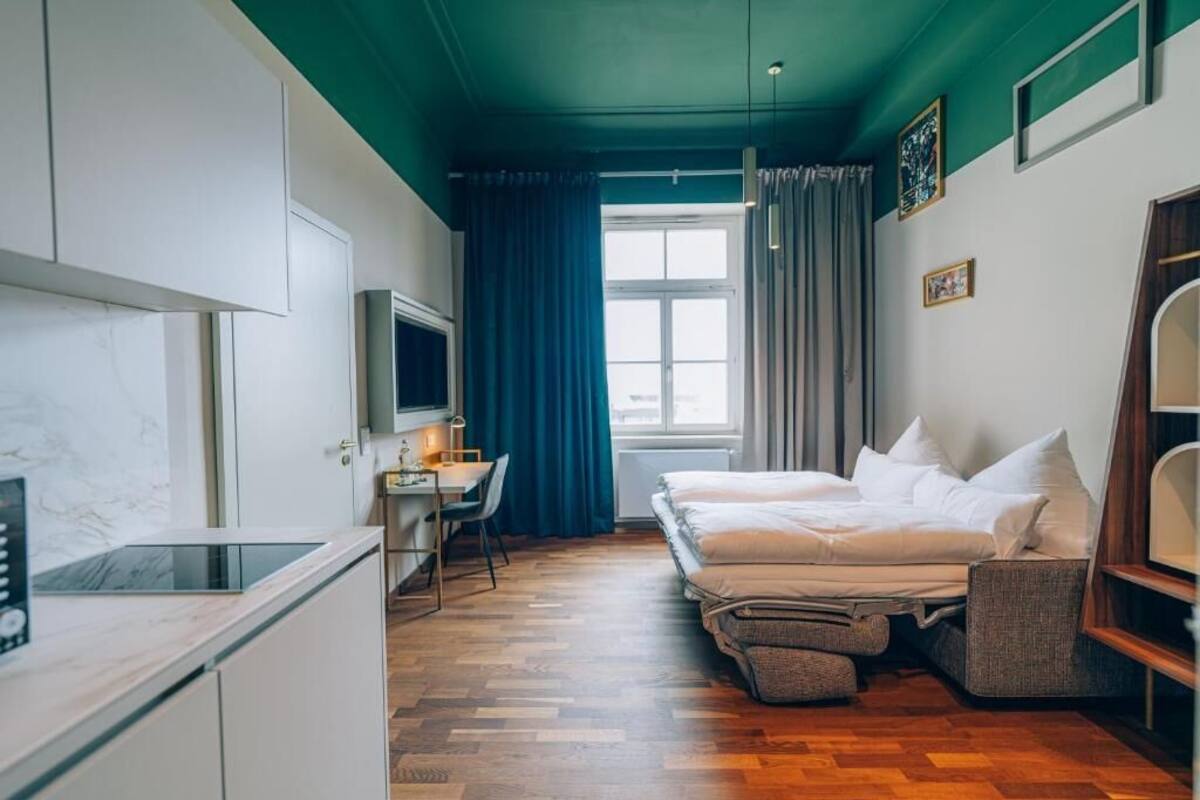 Una habitación pequeña con cama, escritorio, televisión y ventana con cortinas.