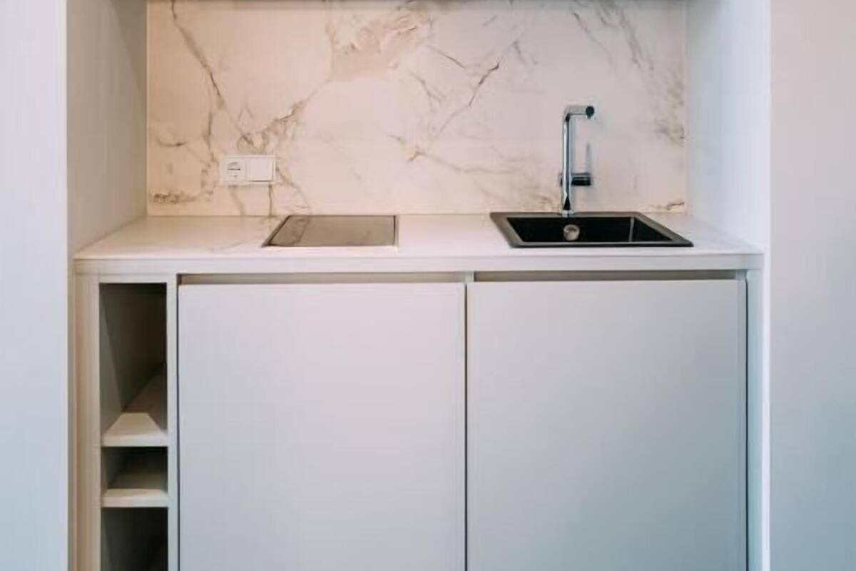 Cocina compacta con gabinetes blancos, salpicadero de mármol y un solo lavamanos.