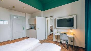 Habitación de hotel con dos camas, un escritorio con silla, televisión montada en la pared y una zona de kitchenette.
